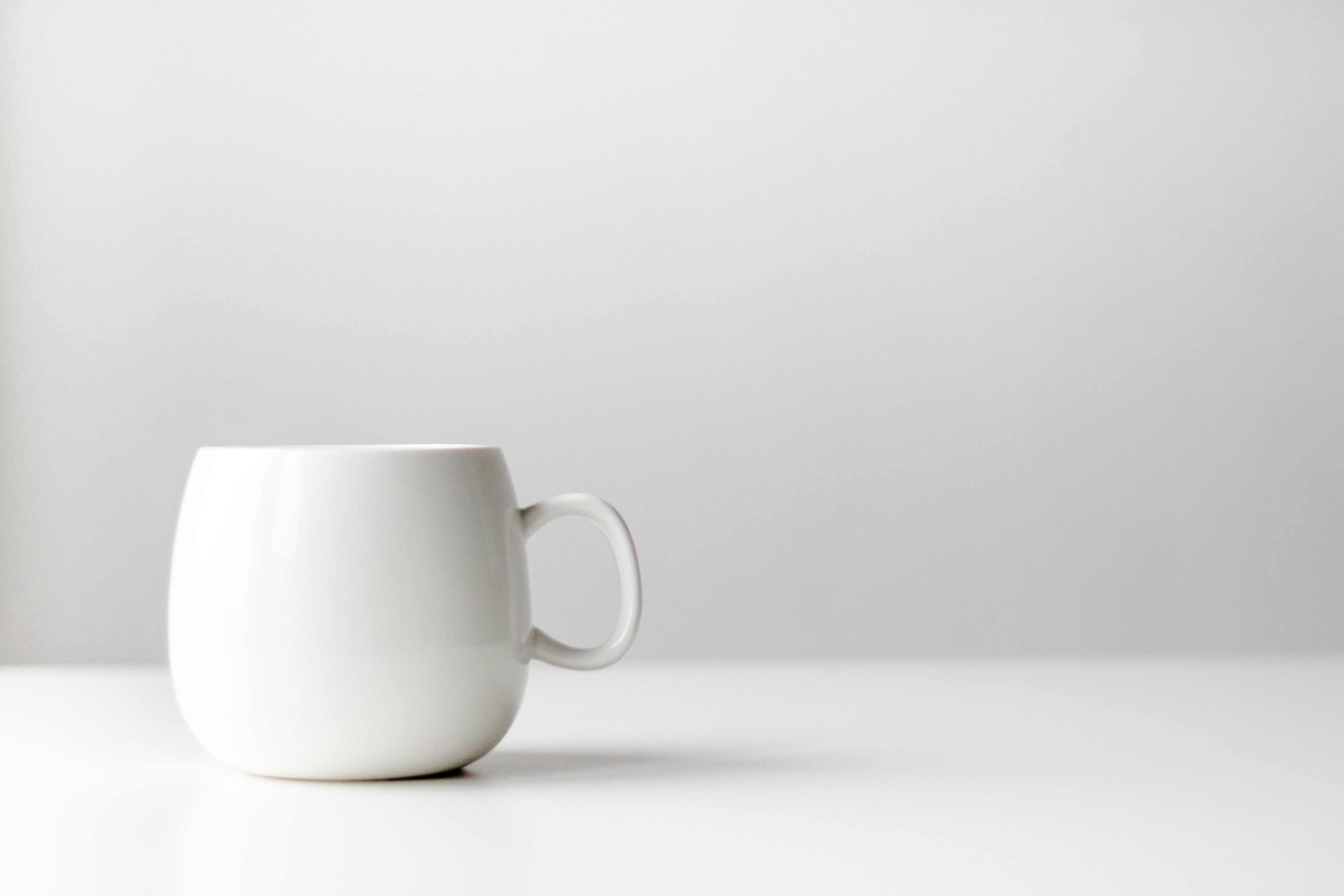 Фотореалистичное изображение белой чашки на белом столе.